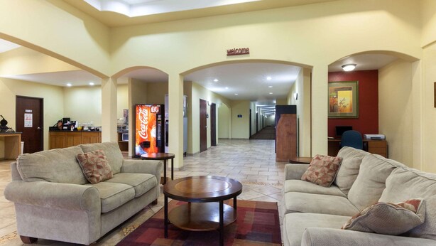 A hotel lobby with two sofas, a coffee table, a Coca-Cola refrigerator, and a 'welcome' sign. - Days Inn by Wyndham San Antonio at Palo Alto (San Antonio)