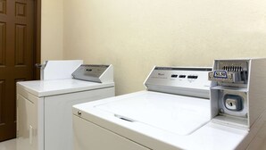 A laundry area with two white washers and dryers, a wooden door, and a wall-mounted coin slot with a $1.50 fee. - Days Inn by Wyndham San Antonio at Palo Alto (San Antonio)
