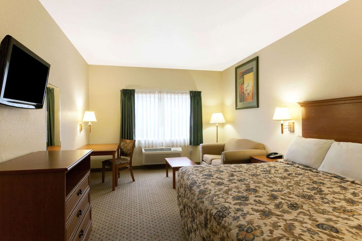 Ein Hotelzimmer mit Bett, Schreibtisch, Stuhl, Fernseher, Lampen und einem Fenster mit Vorhängen.