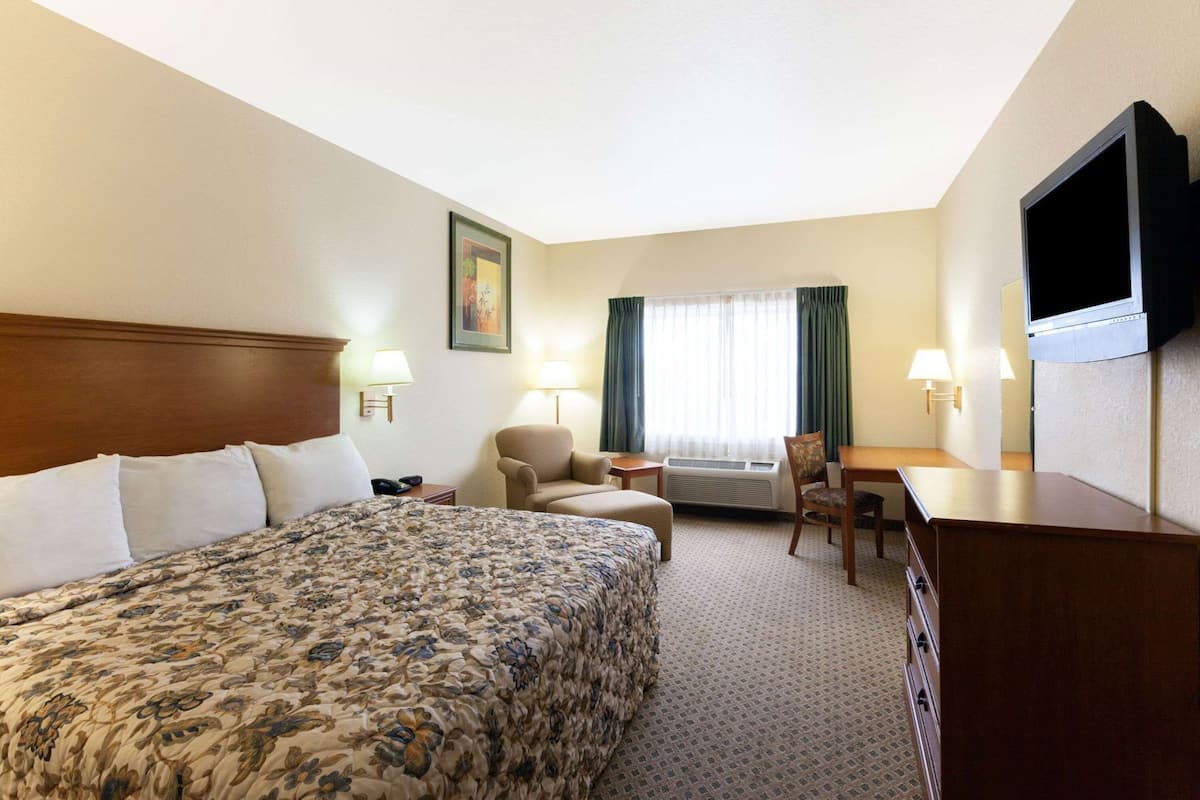 Ein Hotelzimmer mit einem großen Bett, einem Schreibtisch, einem Stuhl, einem Fernseher und einem Fenster mit Vorhängen.