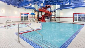 An indoor swimming pool with a red water slide, tiled flooring, and a pool ladder. - Ramada by Wyndham Pincher Creek (Pincher Creek)