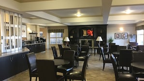 A restaurant with a bar area, multiple tables and chairs, and a television screen. - Ramada by Wyndham Pincher Creek (Pincher Creek)