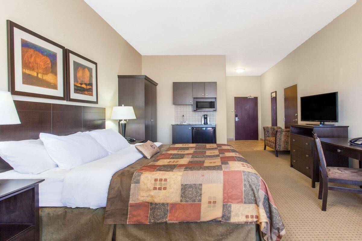 Una habitación de hotel con cama, escritorio, televisión, microondas y kitchenette.