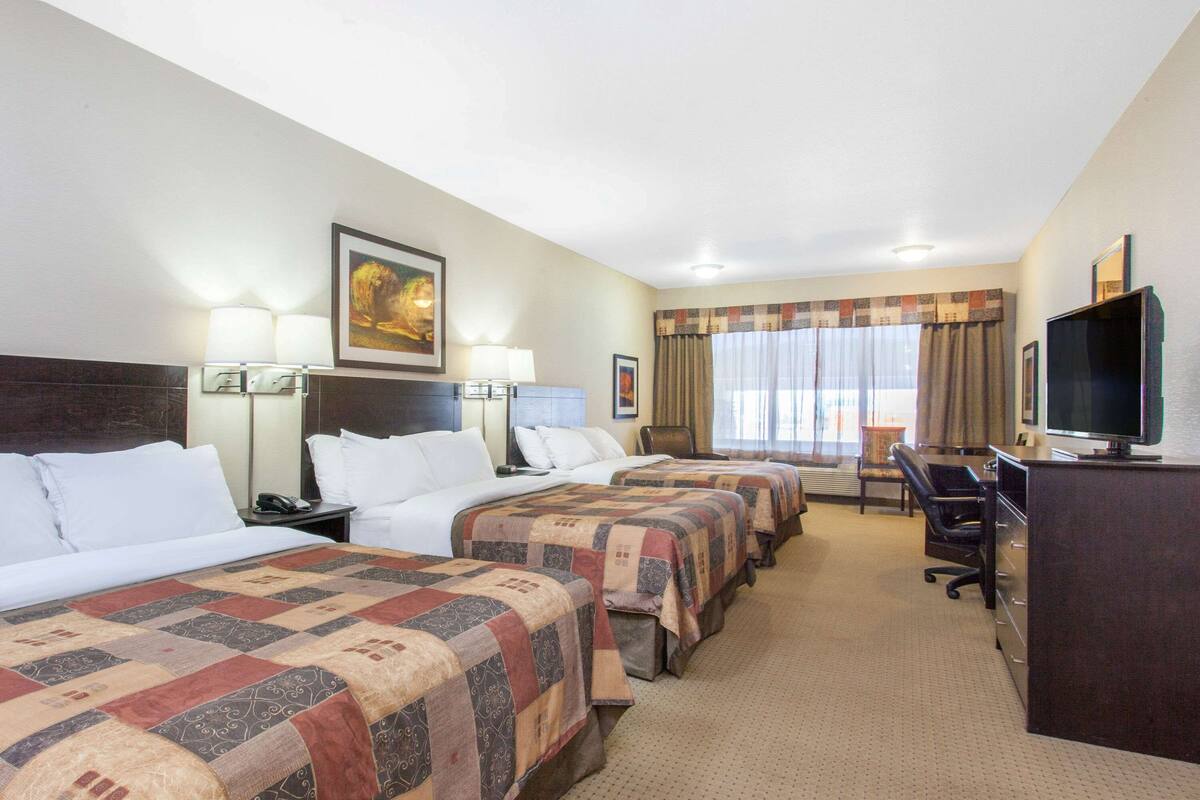 Habitación de hotel con tres camas, un escritorio con televisor y una ventana con cortinas.