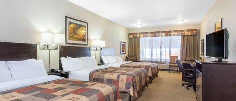 A hotel room with three beds, a desk with a television, and a window with curtains.