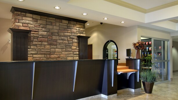 A reception area with a stone wall, a wooden reception desk, and a potted plant. - Ramada by Wyndham Pincher Creek (Pincher Creek)