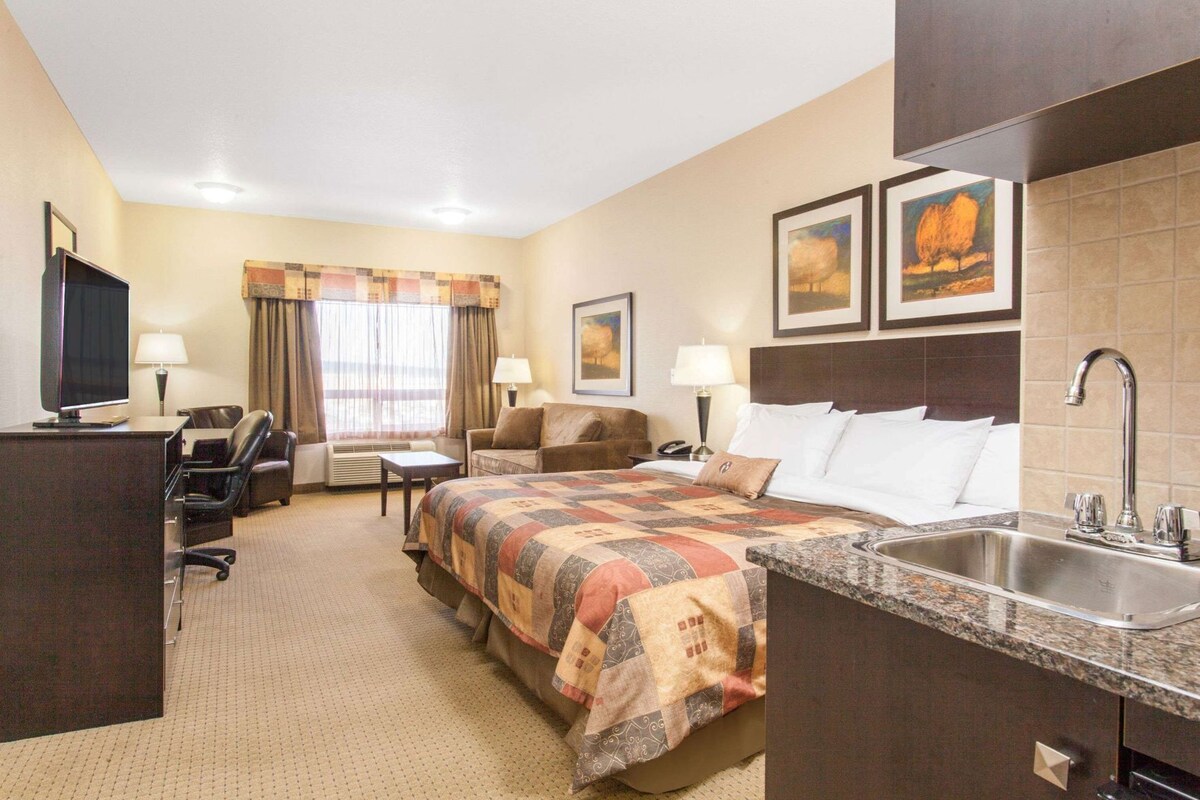 Una habitación de hotel con cama, escritorio, silla, televisor y lavamanos.