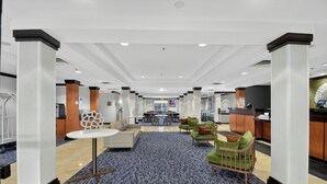Un amplio vestíbulo de hotel con una zona de estar central, una recepción y vistas al área de comedor al fondo.