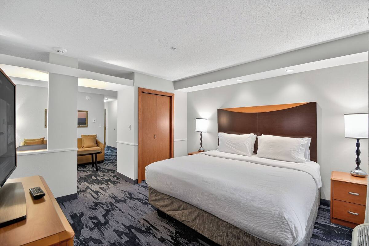 Quarto de hotel com uma cama grande, televisão, escrivaninha e sofá.