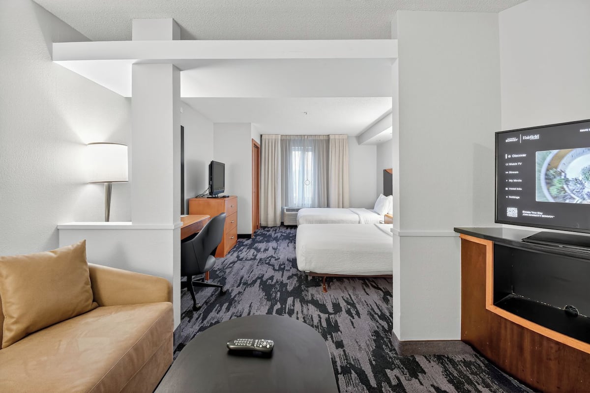 Quarto de hotel com cama, escrivaninha, televisão, controle remoto e abajur.