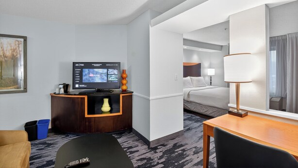 Habitación de hotel con televisión, escritorio, silla, cama y baño visible a través de una puerta abierta.