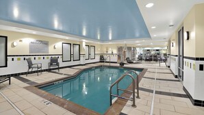 Una piscina interior con suelo de baldosas, sillas de descanso y un cartel con las normas de la piscina.