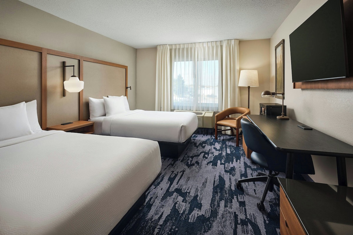 A hotel room with two beds, a desk, a chair, a television, and a window with curtains.