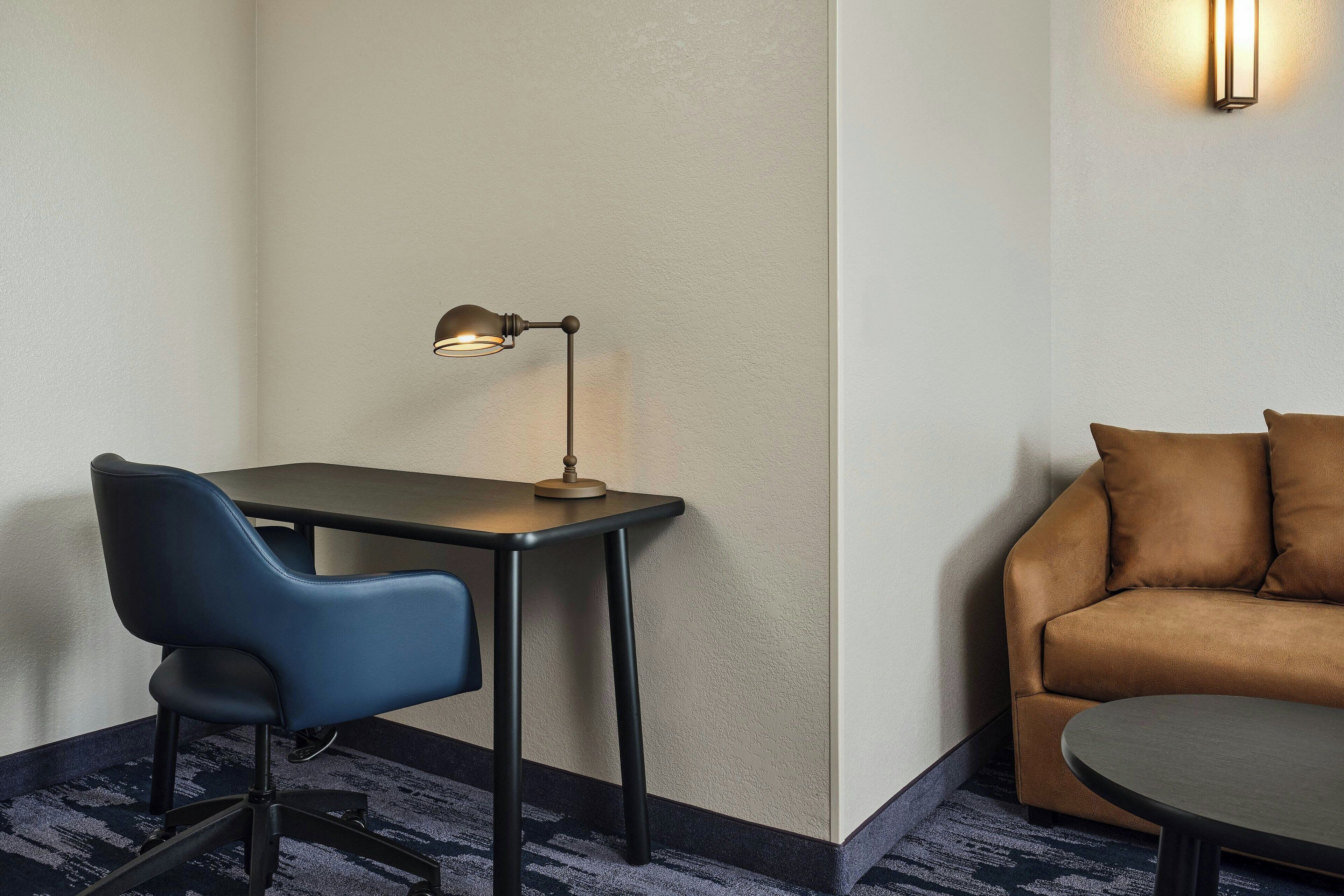 A hotel room with a desk, chair, and sofa.