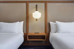 Una habitación de hotel con dos camas, una mesita de noche de madera y una lámpara fijada en la pared.