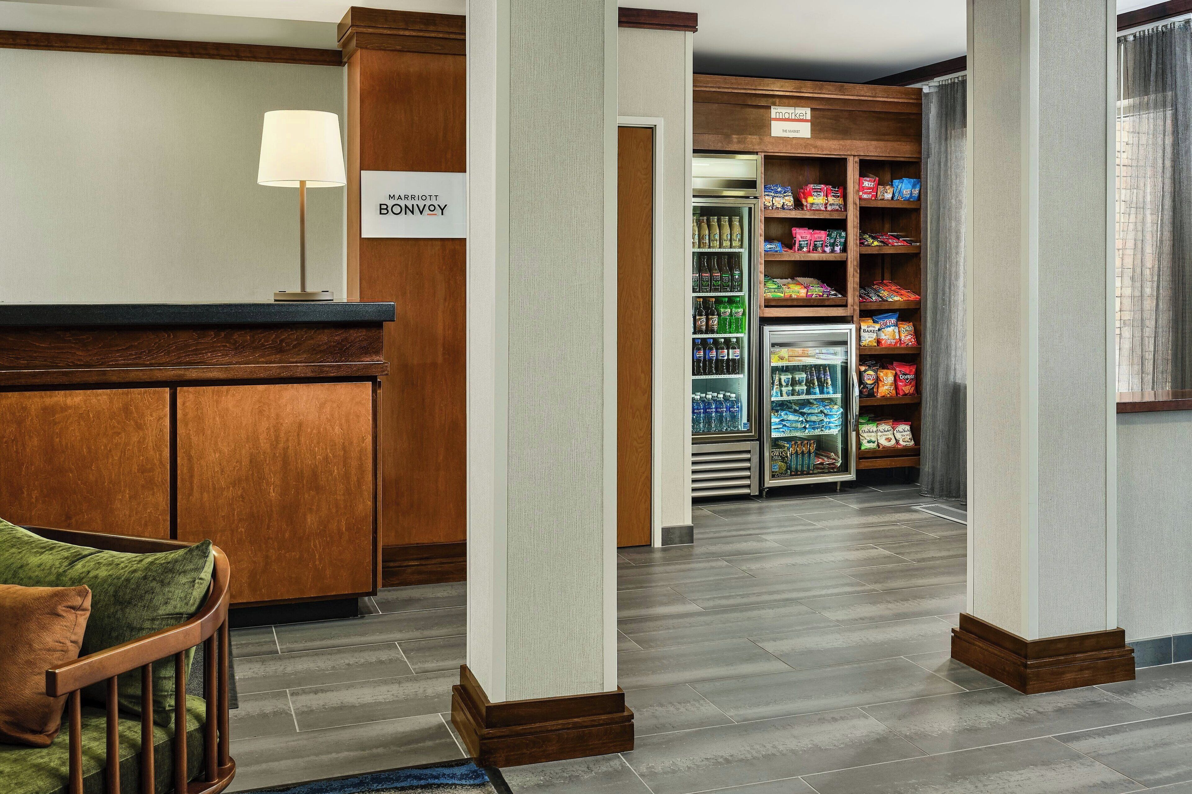 A hotel lobby with a reception desk, a seating area, and a snack bar with various food items.