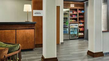 A hotel lobby with a reception desk, a seating area, and a snack bar with various food items.