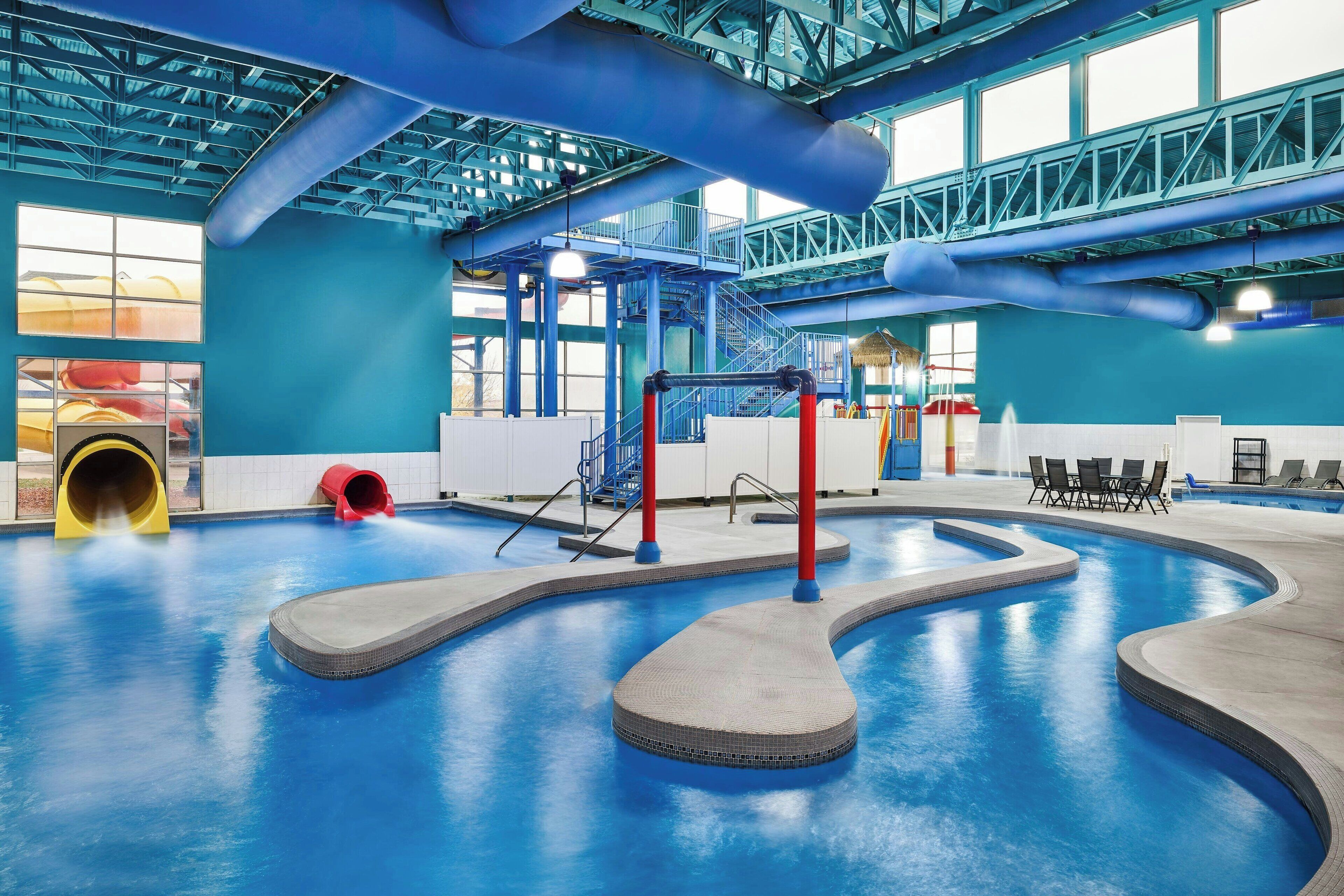 An indoor swimming pool with a blue floor, a red and black water slide, and a yellow slide.