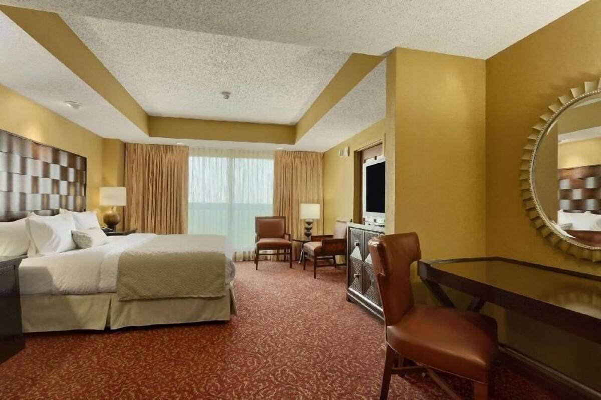 A hotel room with a bed, a desk, a chair, a television, and a large mirror.