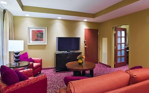 A hotel room with a sofa, armchair, TV, and a small table with a vase. - Embassy Suites by Hilton Nashville SE Murfreesboro (Murfreesboro)