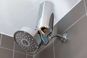 A modern showerhead with a curved design, mounted on a wall with a white textured surface.