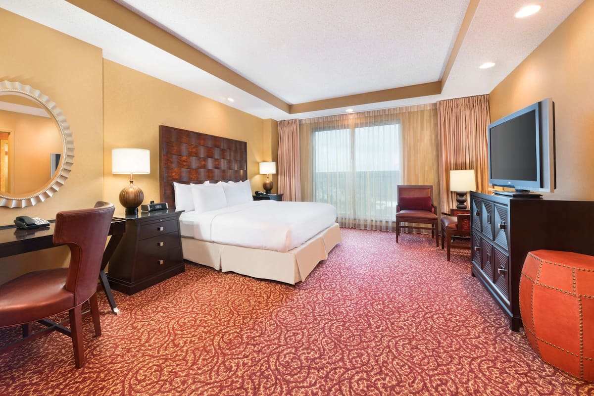 A hotel room with a large bed, a desk with a chair, a TV, and a red patterned carpet.