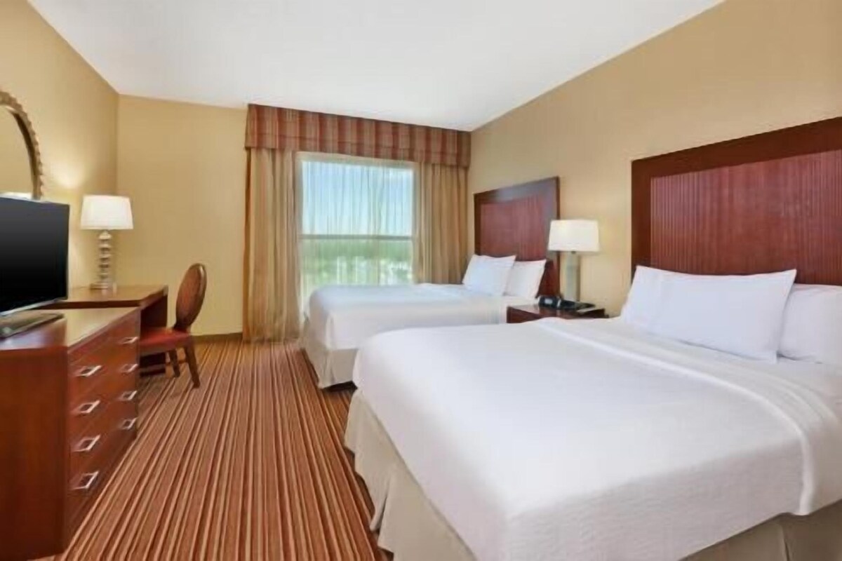 A hotel room with two beds, a desk with a TV, and a window with curtains.