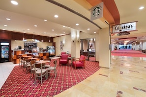 A hotel lobby with a Starbucks coffee shop, seating area, and a vending machine.