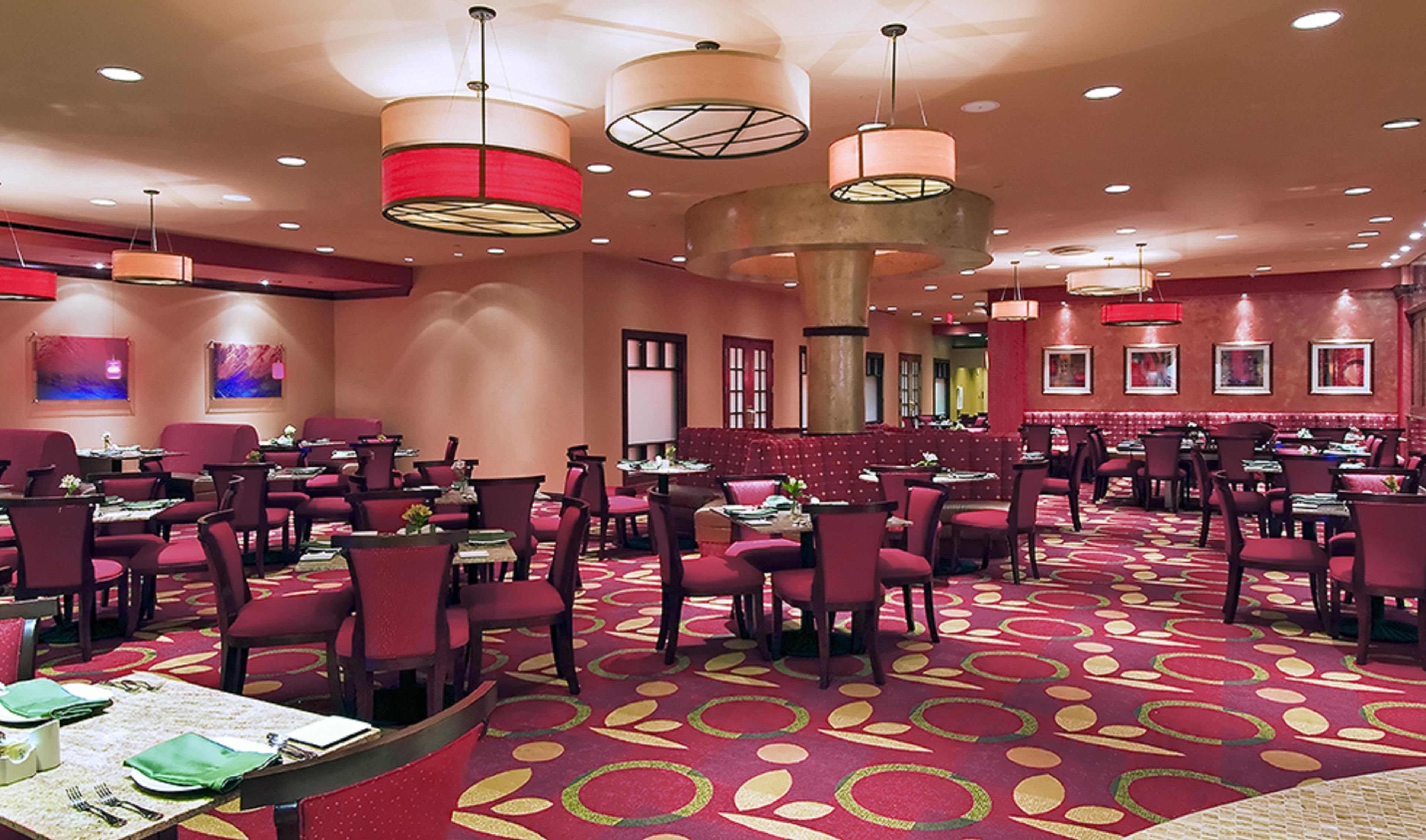 A hotel dining area with multiple tables and chairs, round tables, and a patterned carpet.