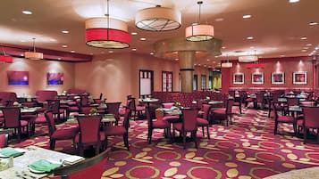 A hotel dining area with multiple tables and chairs, round tables, and a patterned carpet.