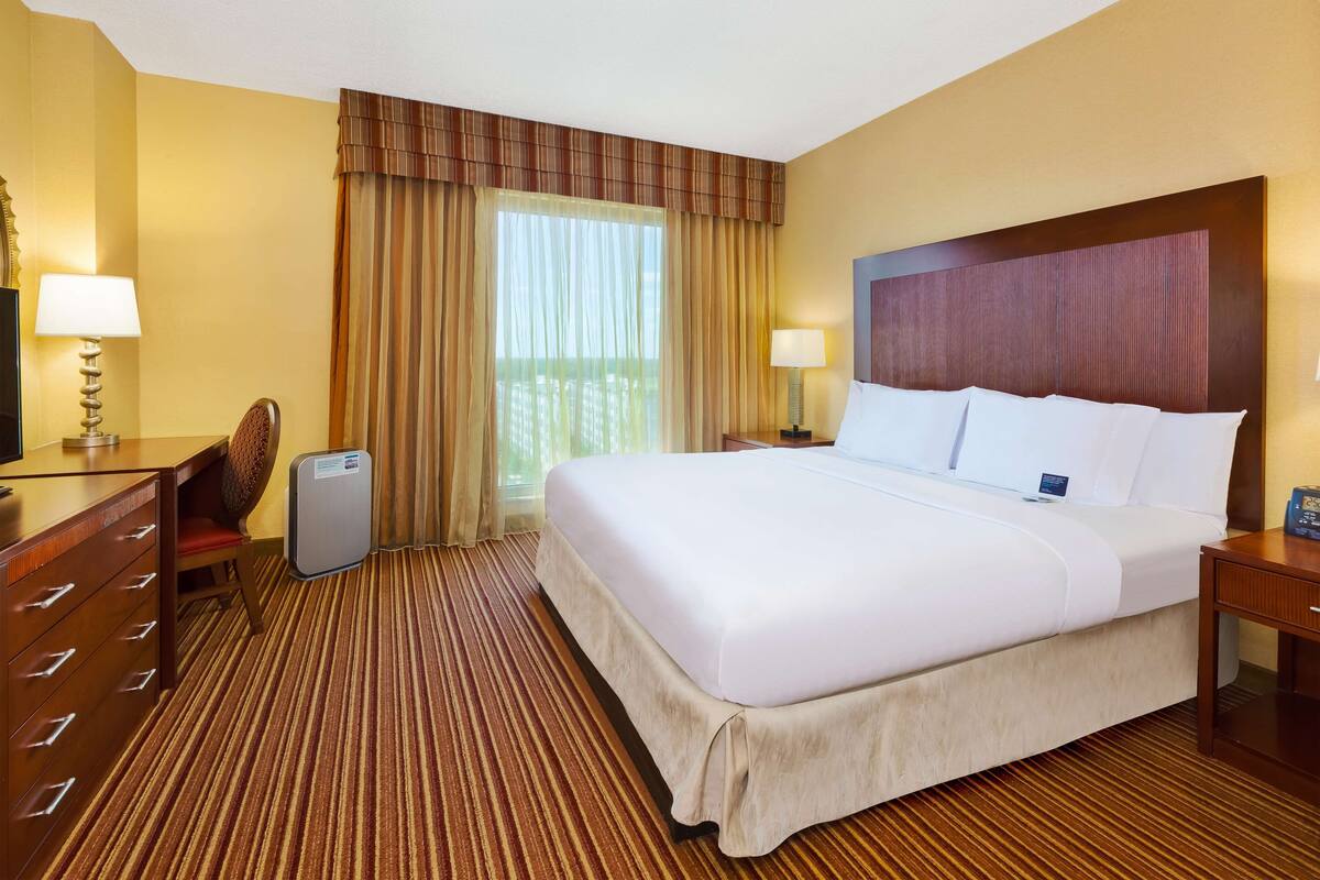 A hotel room with a large bed, a desk with a chair, a dresser, and a window with curtains.