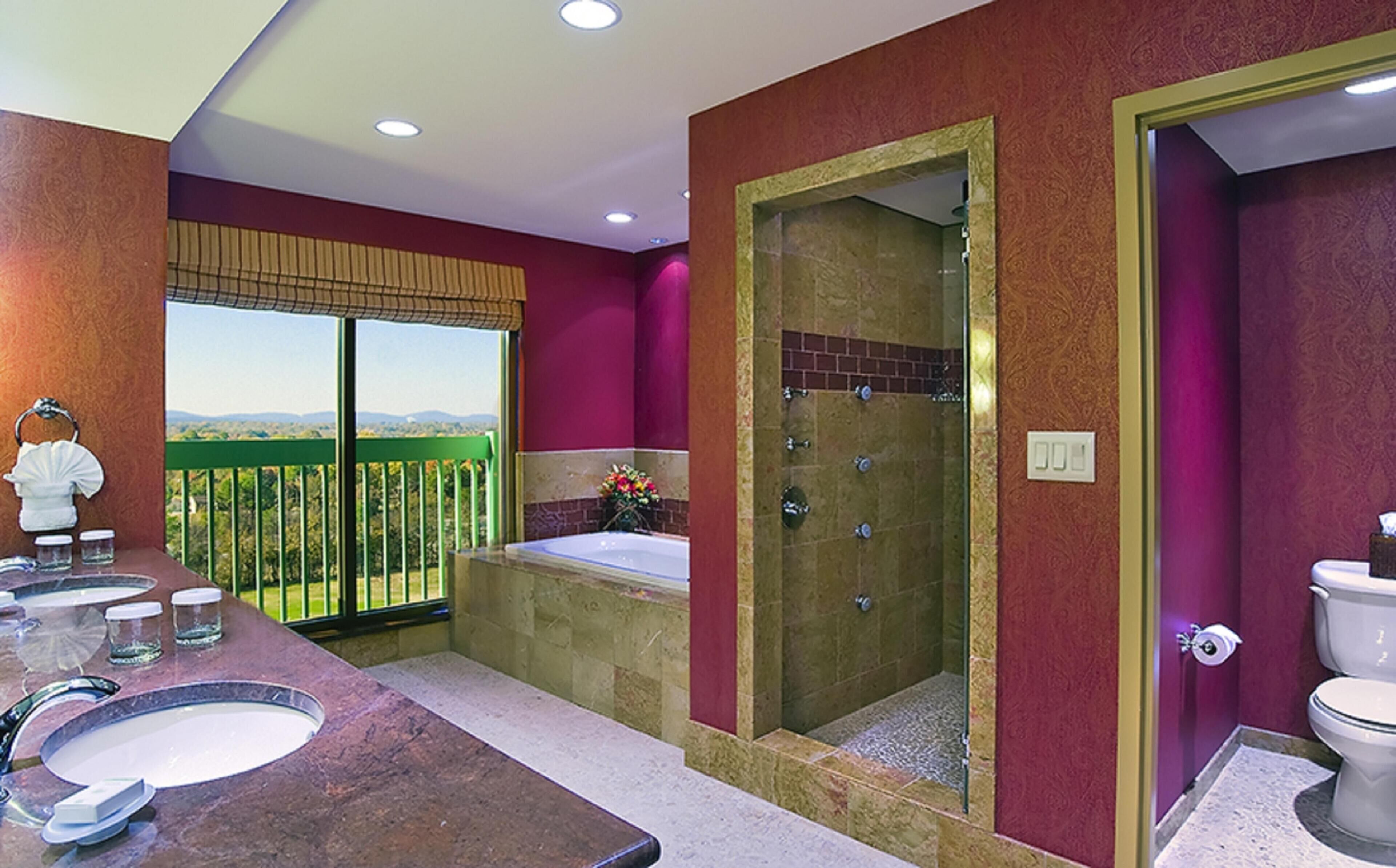 A bathroom with a large bathtub, a shower, and a toilet. There is a window with a view of greenery.