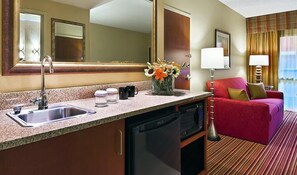 Habitación de hotel con cocina, un sofá rojo, un espejo grande y una ventana con cortinas.