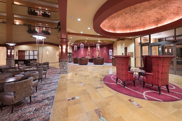 A spacious lobby with multiple seating areas, including round tables and chairs, and a large, circular red carpet.