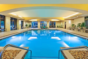 A large indoor swimming pool with a tiled edge, surrounded by seating areas and potted plants.