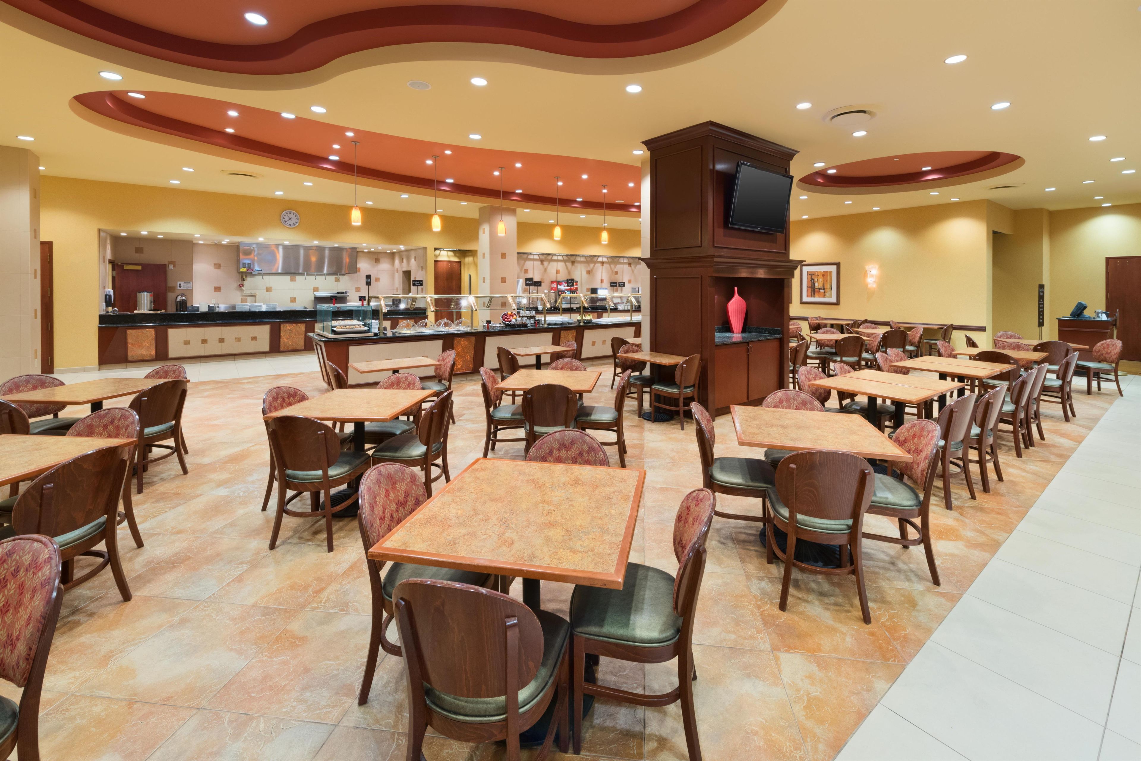 A spacious dining area with multiple tables and chairs, a buffet counter, and a television screen.