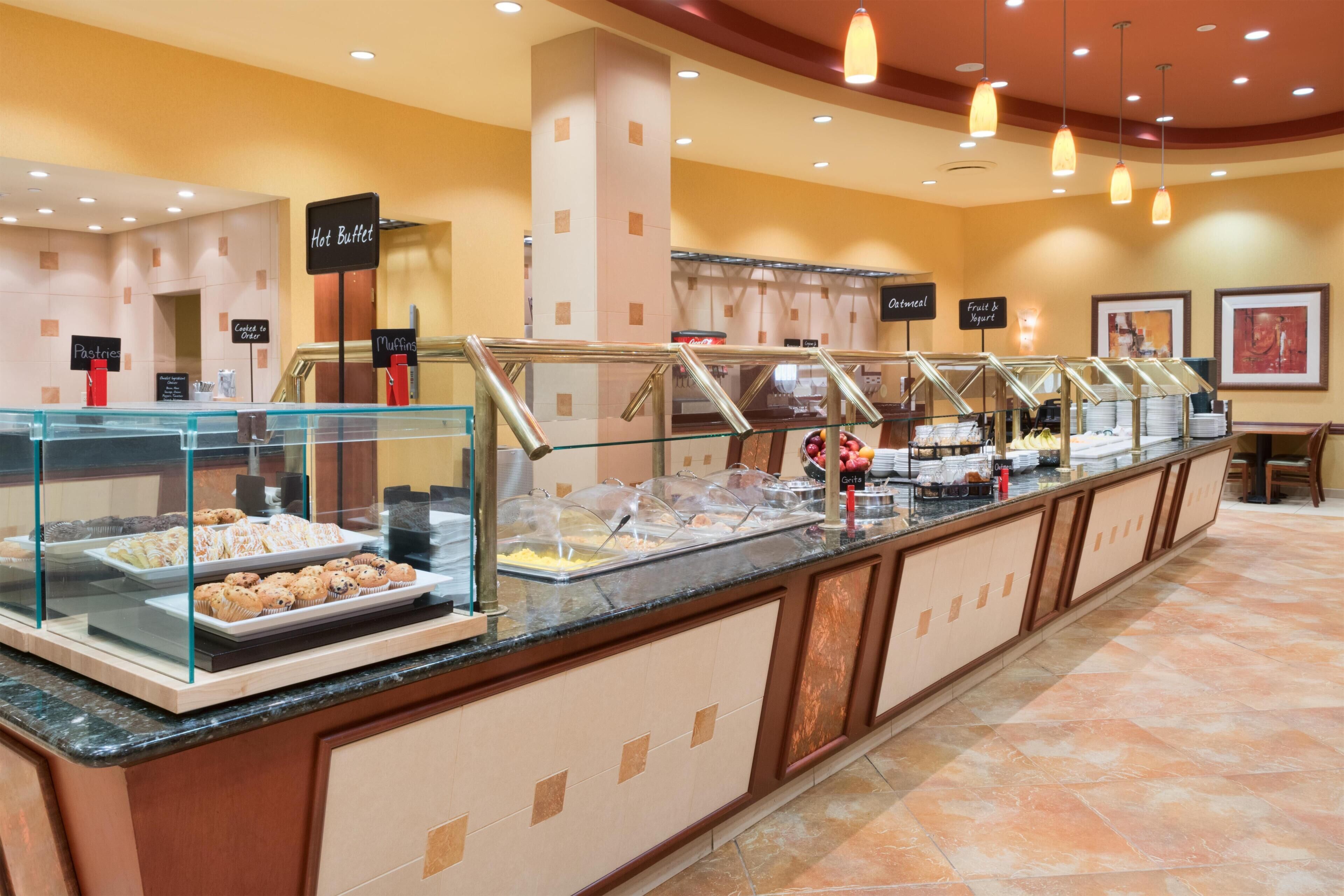 Zona de bufé con señalización clara para la sección de alimentos calientes, muffins, pasteles, avena, fruta y yogur, y preparados de maíz.