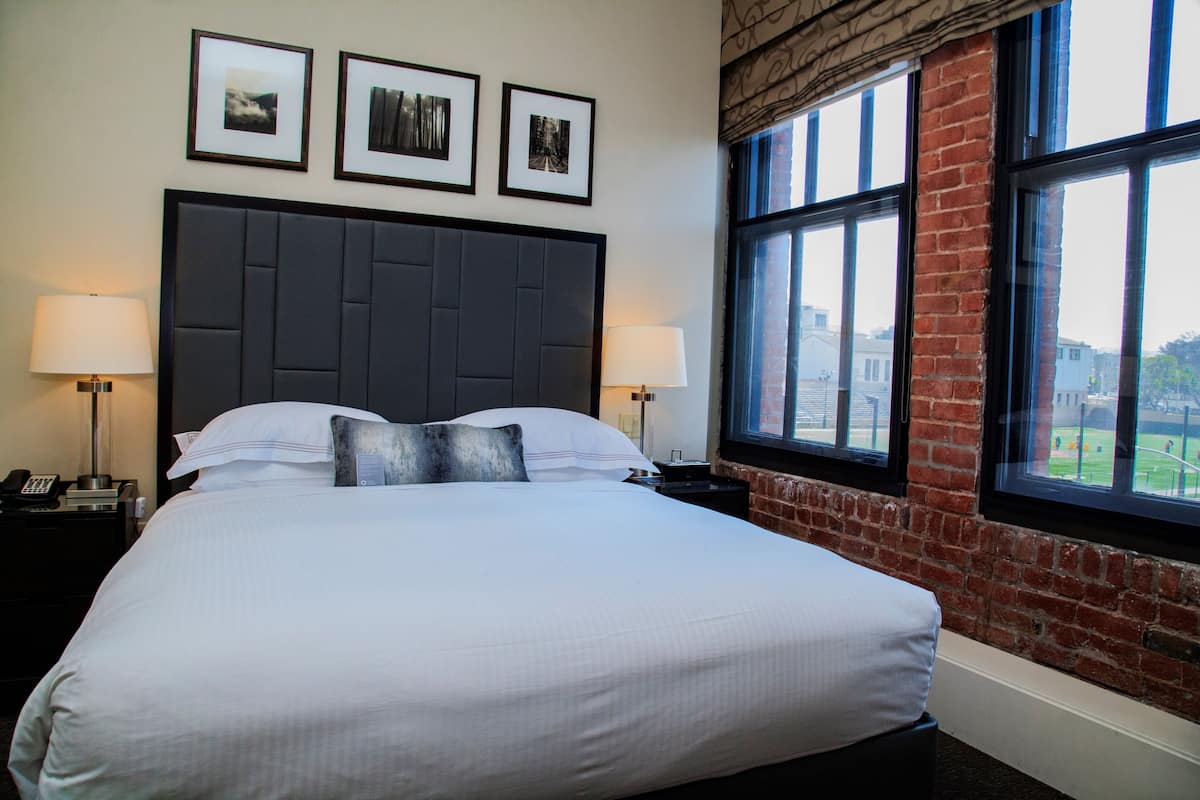 A neatly made bed with a dark headboard, two bedside lamps, and three framed pictures on the wall.