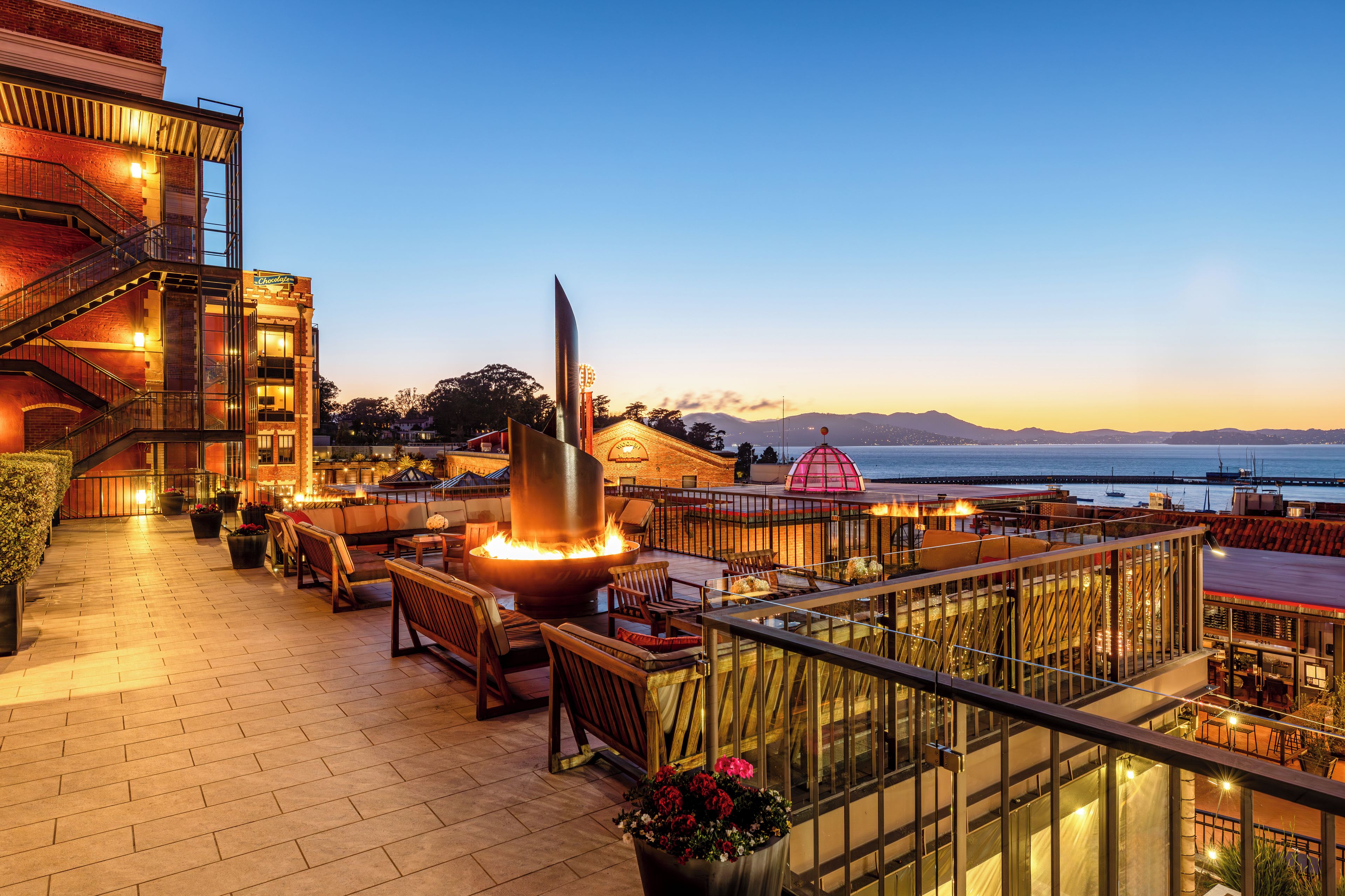 Eine Dachterrasse mit Sitzgelegenheiten im Freien, einer Feuerstelle und Blick auf das Meer.
