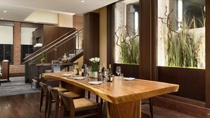A modern dining area with a long wooden table set for six, surrounded by wooden chairs. A staircase with a metal railing is visible in the background. - Fairmont Heritage Place, Ghirardelli Square (San Francisco)