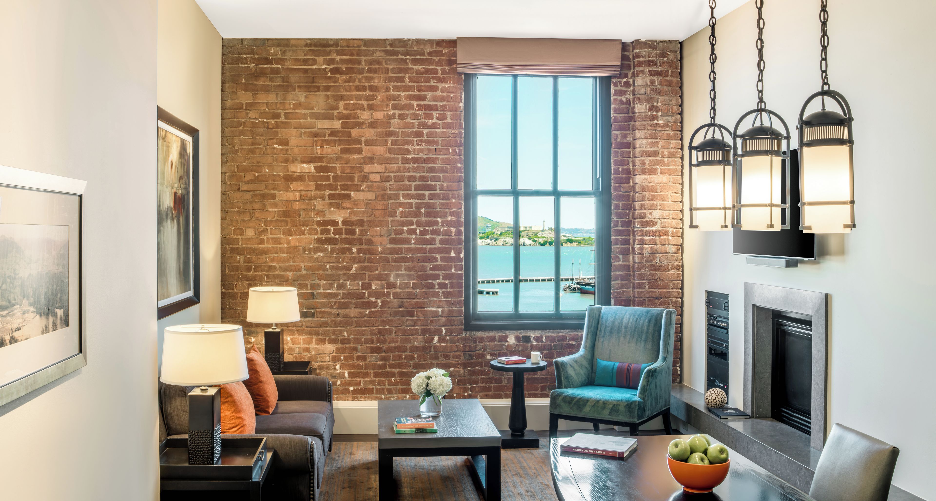 Ein Wohnzimmer mit Backsteinwand, großem Fenster mit Blick auf das Wasser, Kamin und modernen Möbeln.