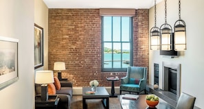 A living room with a brick wall, a large window with a view of the water, a fireplace, and modern furniture. - Fairmont Heritage Place, Ghirardelli Square (San Francisco)