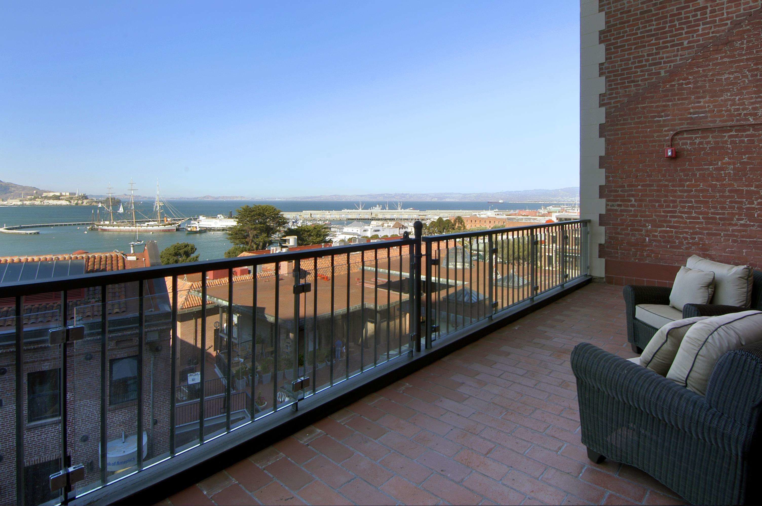 Un balcon avec vue sur la mer, un mur en briques et un canapé en osier.