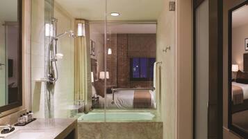 Une salle de bain d’hôtel avec une douche à parois de verre, une baignoire, un lavabo équipé de produits de toilette et un miroir.
