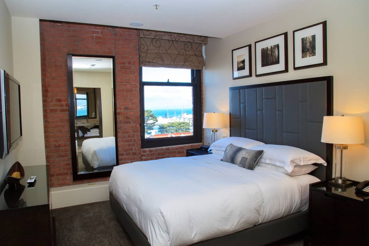 A hotel room with a large bed, a view of the sea, a brick wall, and a mirror.