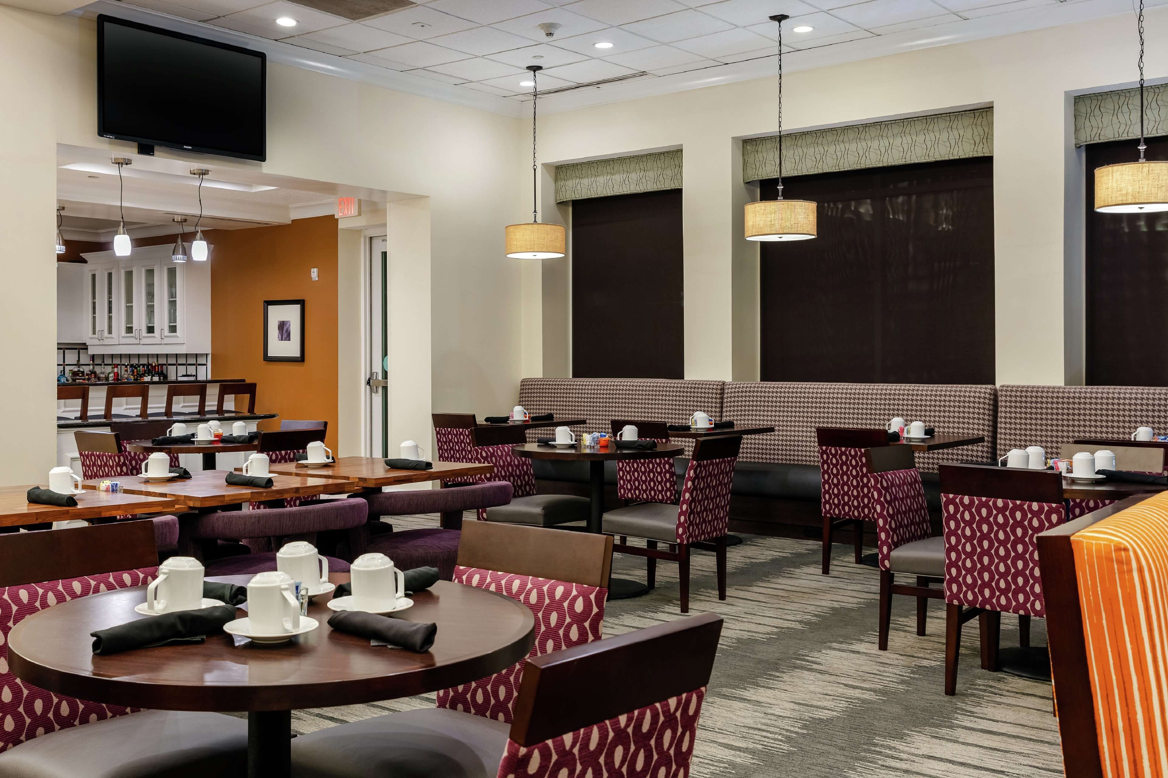 Une salle à manger d'hôtel avec des tables rondes, des chaises à motifs et un bar en arrière-plan.