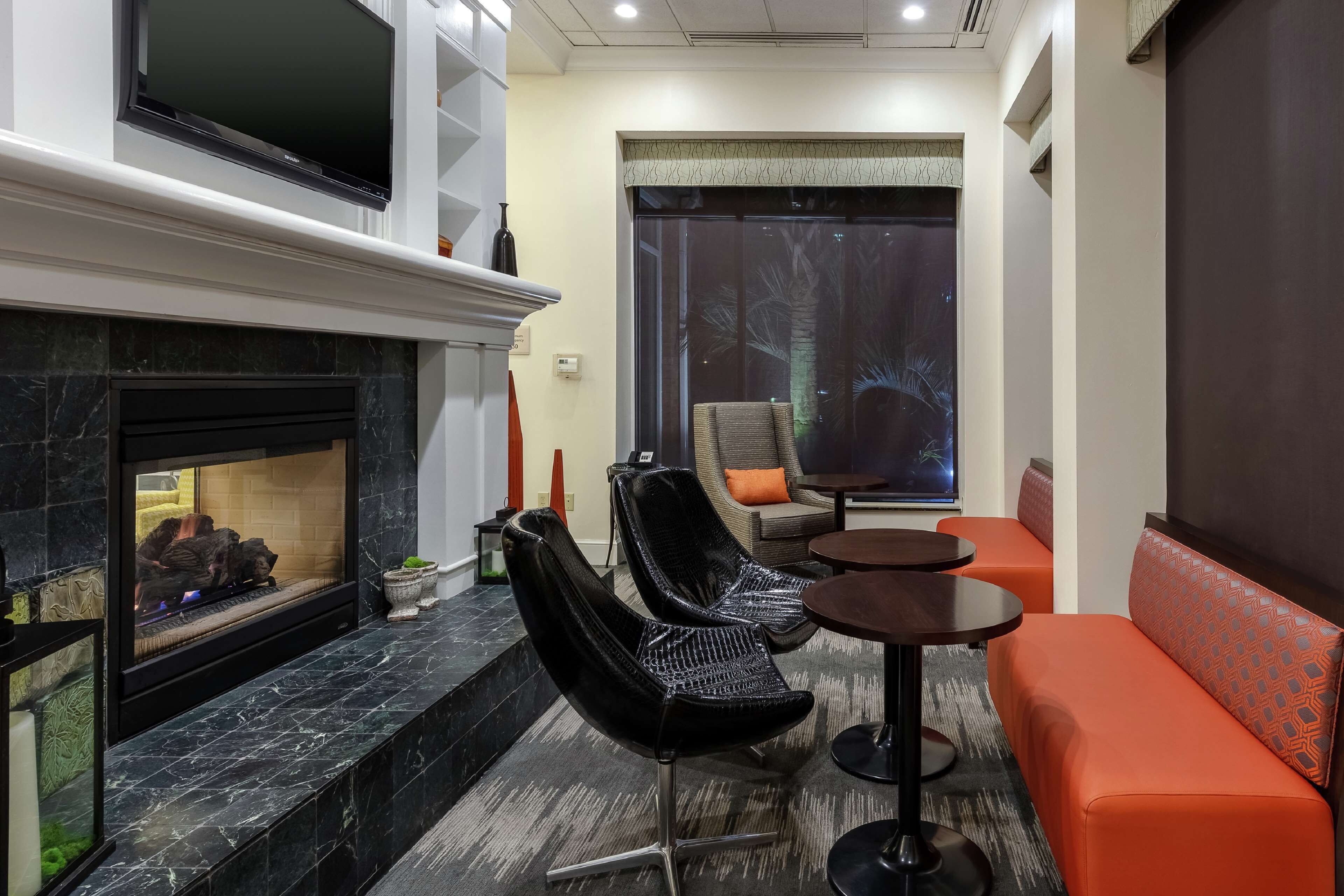 Una sala de estar moderna con chimenea, sillas negras, sofá naranja y televisor montado en la pared.