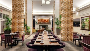 Un vaste espace de salle à manger intérieur, avec une longue table dressée pour un repas, flanqué de hautes colonnes décoratives et éclairé par des luminaires suspendus modernes.