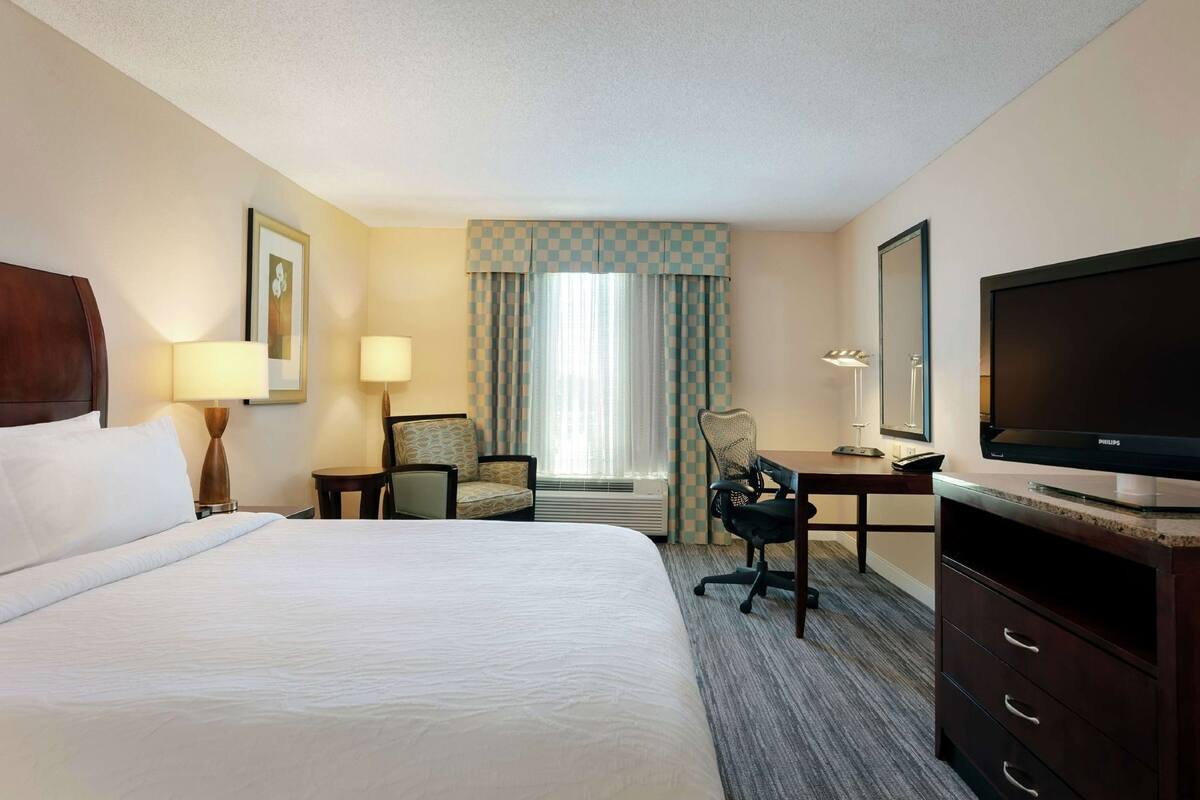 Een hotelkamer met een bed, bureau, stoel, televisie en een raam met gordijnen.