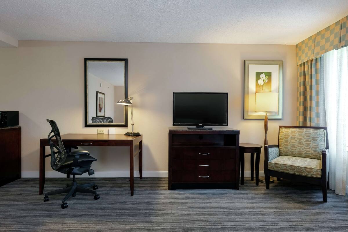 Een hotelkamer met een bureau, stoel, televisie en kunstwerken aan de muur.